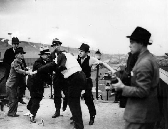 The surviving photograph of the Battle of the Overpass. From left to right: Tellford, unidentified, Angelo Caruso, Commett, Goodman, Frankensteen (with his jacket pulled over his head), and photographers on the far right. (Courtesy of the Zinn Education Pr